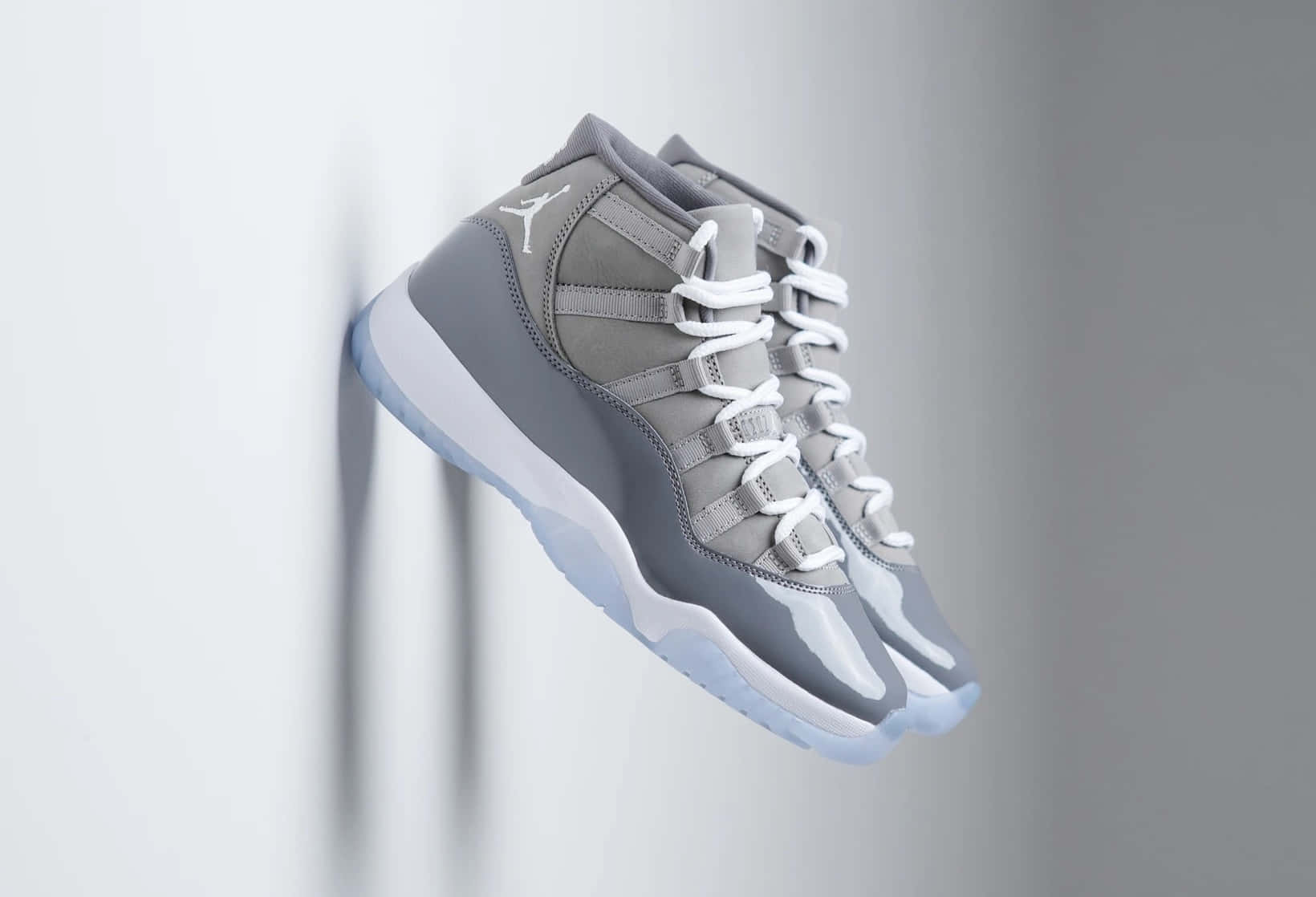 Cool Gray 桌布 壁紙 — 一雙灰色Jordan 11運動鞋，搭配白色鞋帶和半透明鞋底，懸掛在極簡灰色牆壁上。