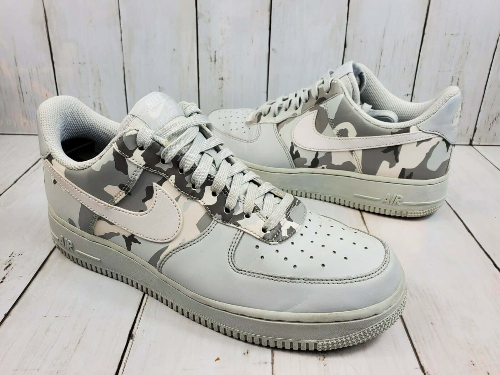 Nike Air Force 桌布 壁紙 — 一雙灰色迷彩Nike Air Force 1運動鞋放在經風化的白色木地板上。