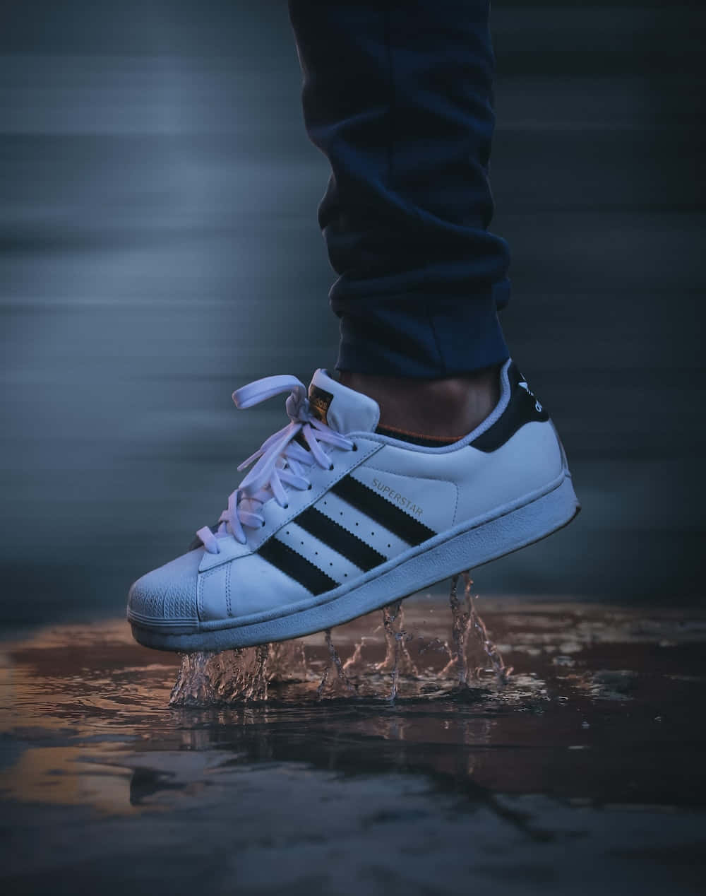 愛迪達 桌布 壁紙 — 一雙白色 adidas superstar 運動鞋在淺水中濺起水花，水滴在空中凝固，背景模糊黑暗。