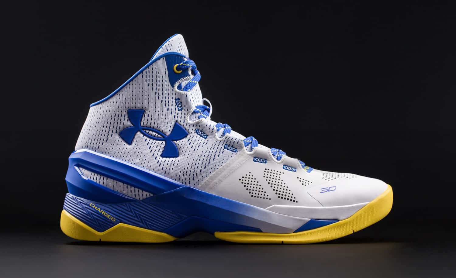 Under Armour 桌布 壁紙 — 一雙白色、藍色和黃色的Under Armour籃球鞋，帶有穿孔網眼和醒目品牌標誌，背景為黑色。