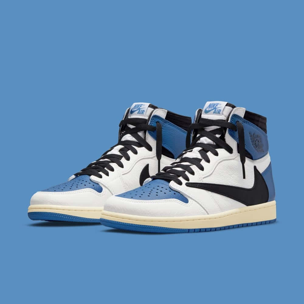 Travis Scott Jordan 1 桌布 壁紙 — 一雙白色、藍色和黑色的高筒運動鞋，搭配奶油色鞋底，置於純藍色背景前。