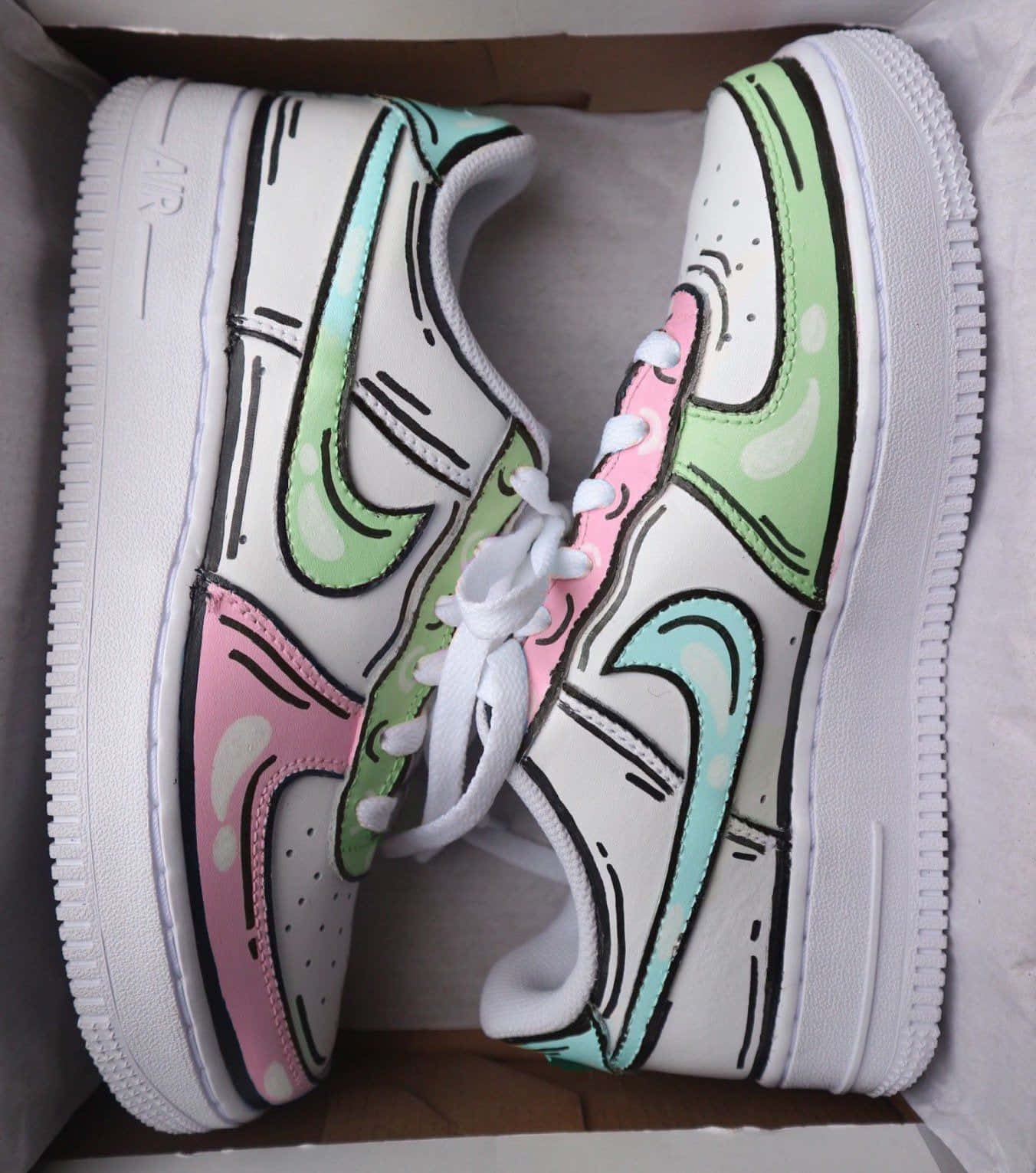 Nike Air Force 桌布 壁紙 — 一雙白色Nike Air Force 1運動鞋，帶有手繪粉彩粉紅、綠色和藍綠色卡通風格點綴，放在鞋盒內。