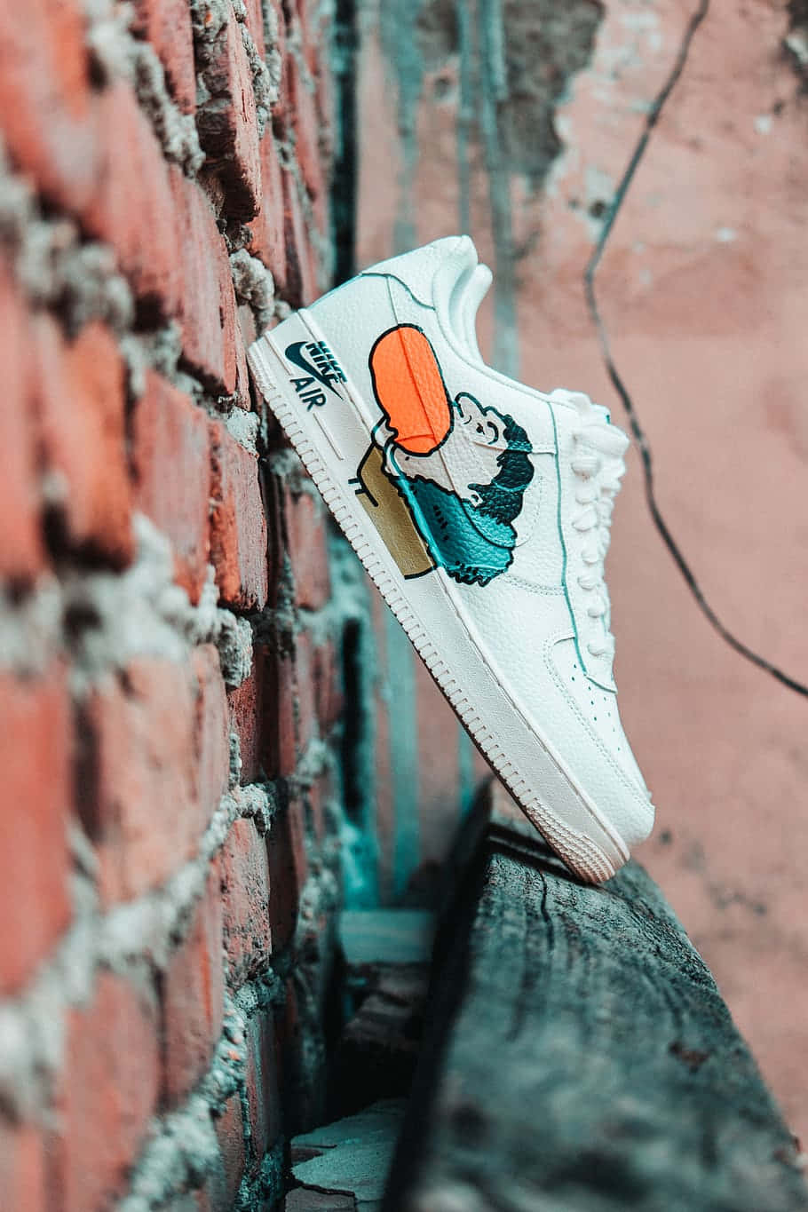 桌布 壁紙 — 一雙白色Nike Air運動鞋，上面有卡通角色拿著橙色氣球，靠在一面風化的紅磚牆上。