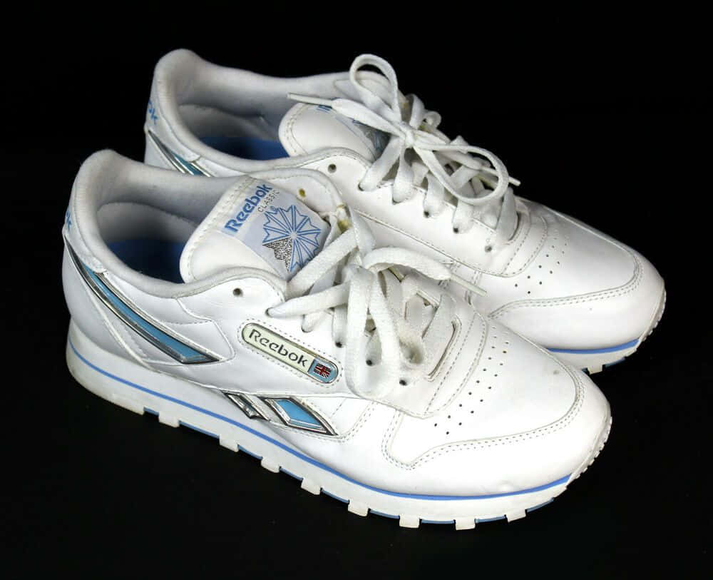 銳步 桌布 壁紙 — 一雙白色Reebok Classic運動鞋，帶有藍色點綴和銀色條紋，置於黑色背景上。