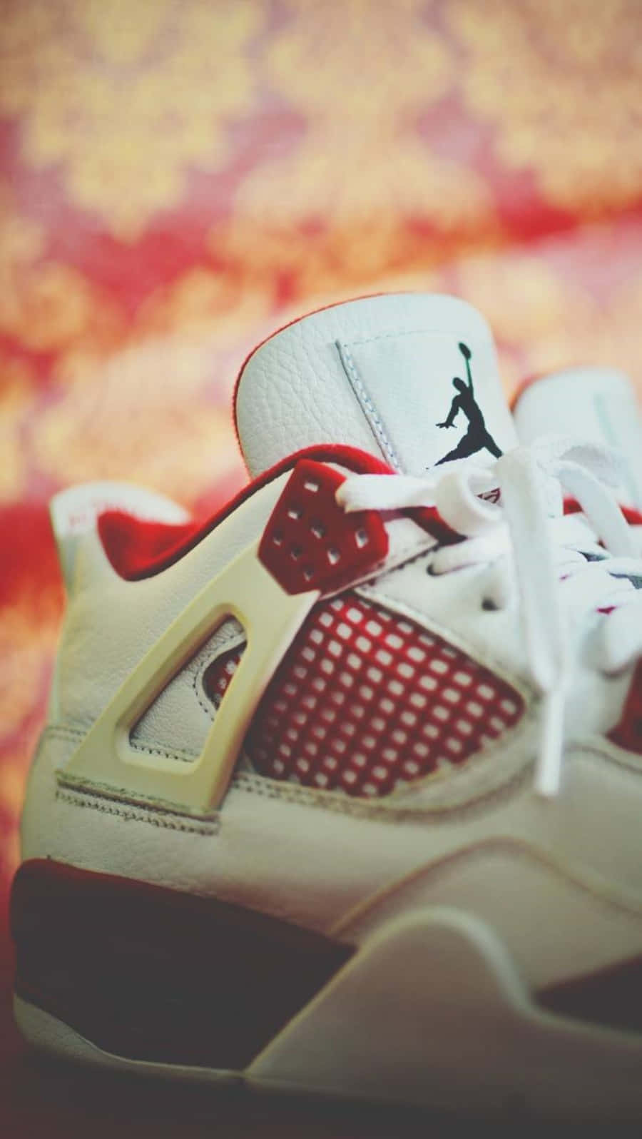 Jordan 4 桌布 壁紙 — 一雙白色和紅色的Jordan 4運動鞋特寫，帶有黑色Jumpman標誌，背景是溫暖模糊的花卉圖案。