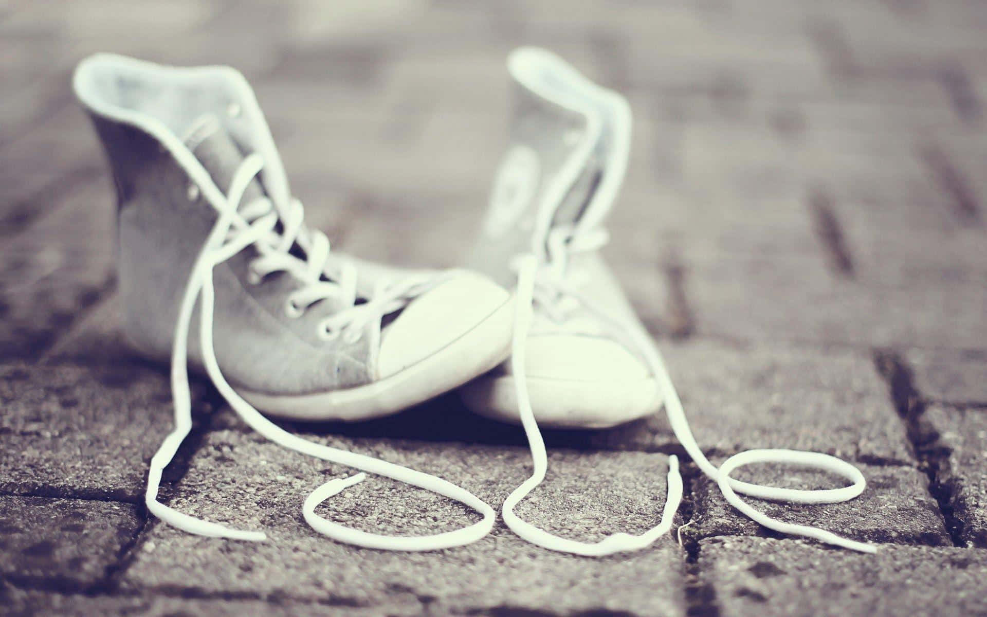 Cute Shoes 桌布 壁紙 — 一雙白色高筒運動鞋，鞋帶鬆開，靜置在風化的鵝卵石街道上，色調柔和低沉。