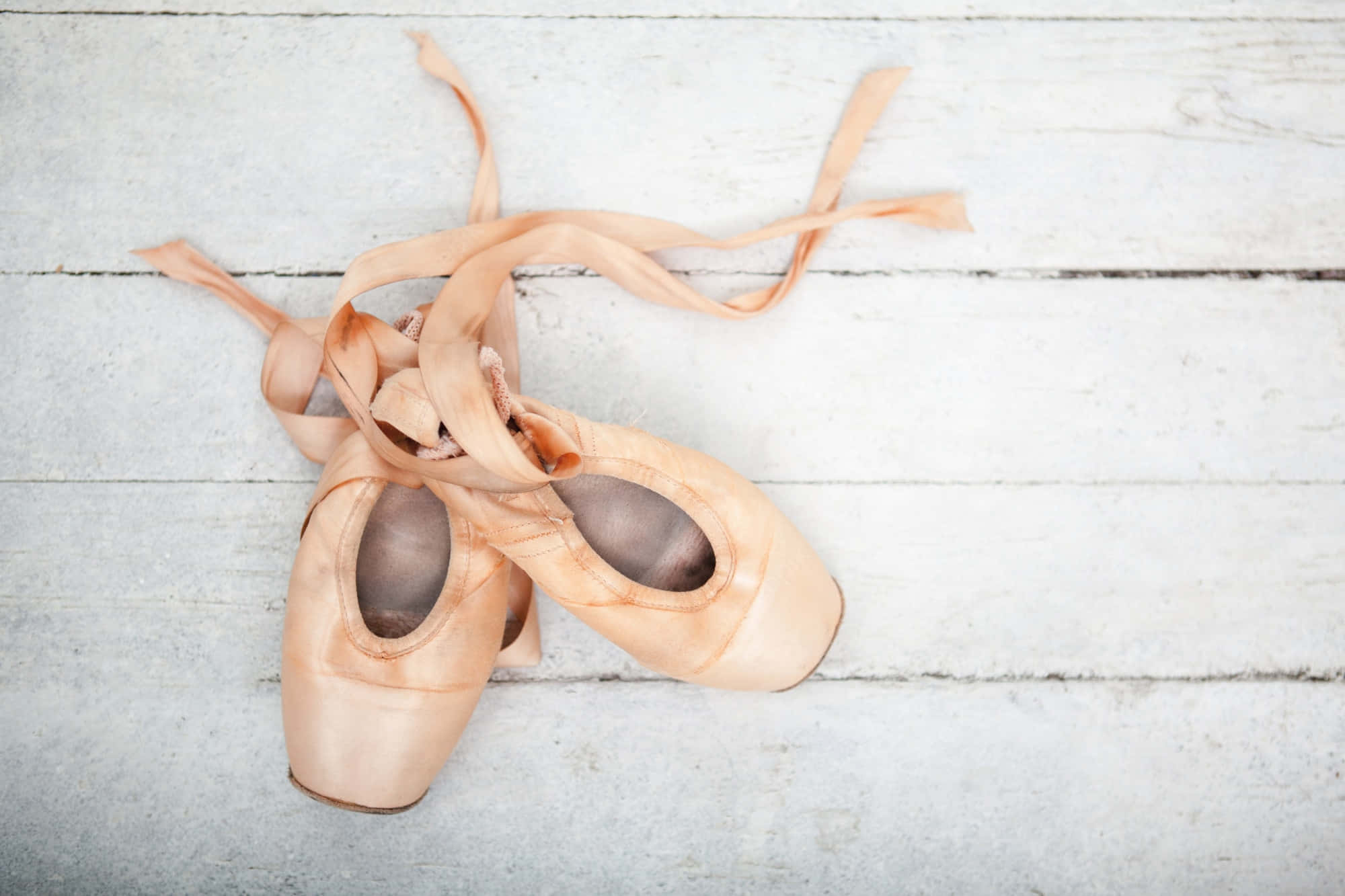 Ballet 桌布 壁紙 — 一雙磨損的桃色芭蕾舞鞋，鞋帶鬆開，擱在風化的白色木地板上。