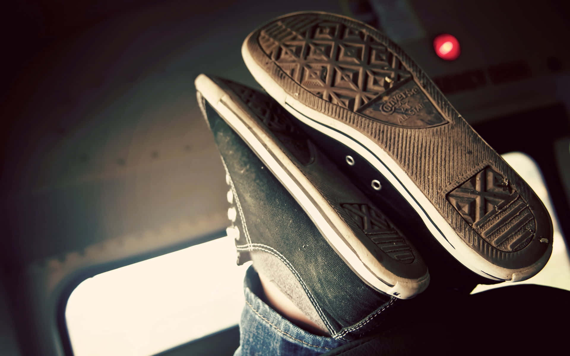 Converse 桌布 壁紙 — 一雙磨損的黑色Converse運動鞋放在穿著牛仔褲的腳上，位於光線昏暗的車內，背景有紅光閃爍。