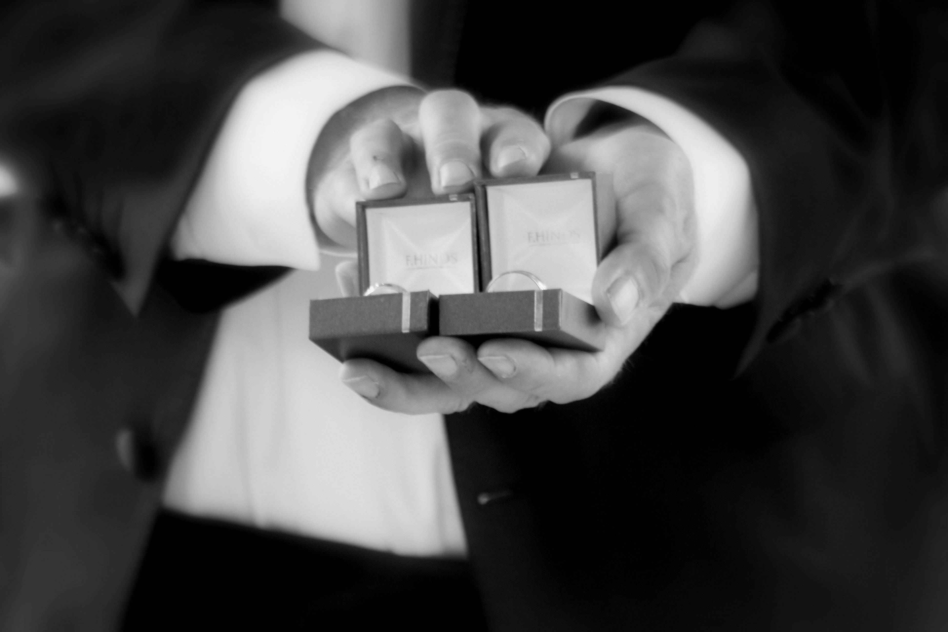 Couple Hands 桌布 壁紙 — 一雙穿著西裝的手，展示兩個打開的戒指盒，內有結婚戒指的黑白特寫。