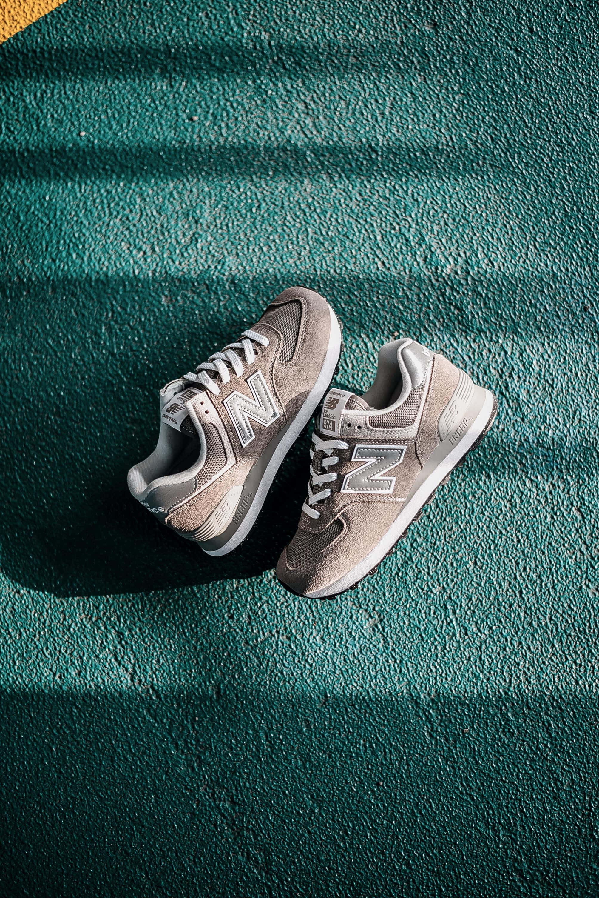 New Balance 桌布 壁紙 — 一雙米色New Balance運動鞋放在有紋理的青綠色表面上，在強烈的斜陽光下投射出銳利的陰影。