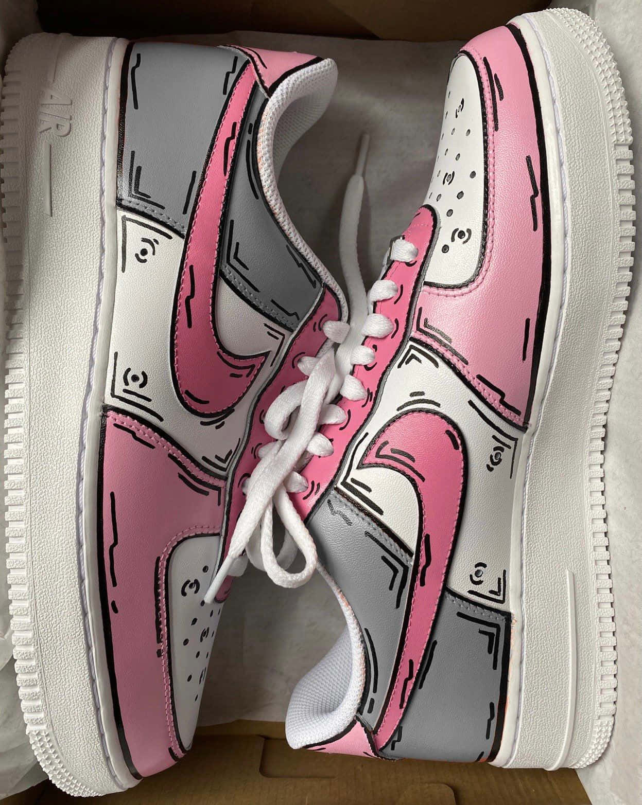 Nike Air Force 桌布 壁紙 — 一雙粉紅色和灰色的運動鞋，帶有卡通風格的黑色輪廓，整齊地放在一個紙板箱裡。