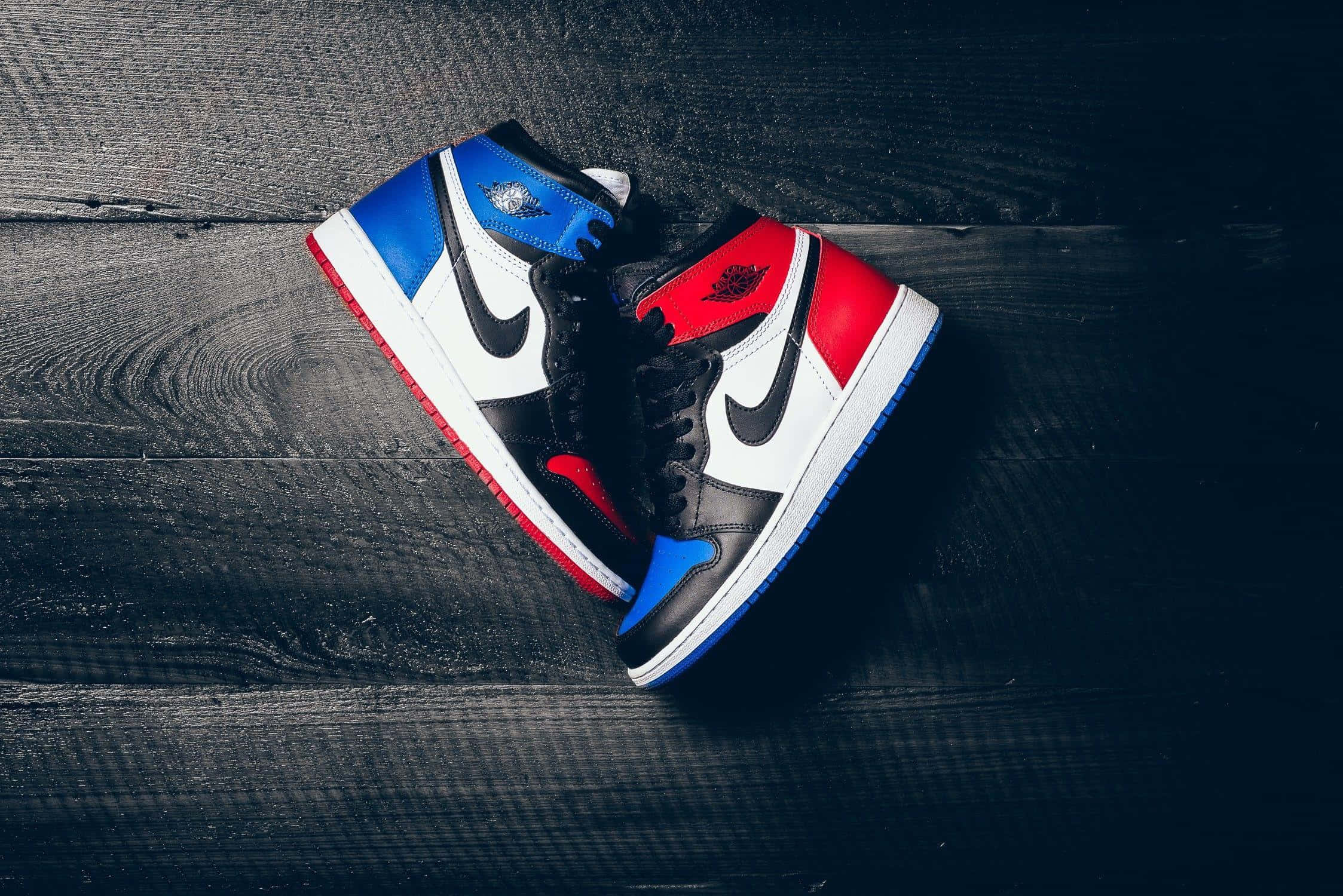 桌布 壁紙 — 一雙紅、藍、黑色 Jordan 1 運動鞋放置在深色紋理木板上，搭配戲劇性燈光。