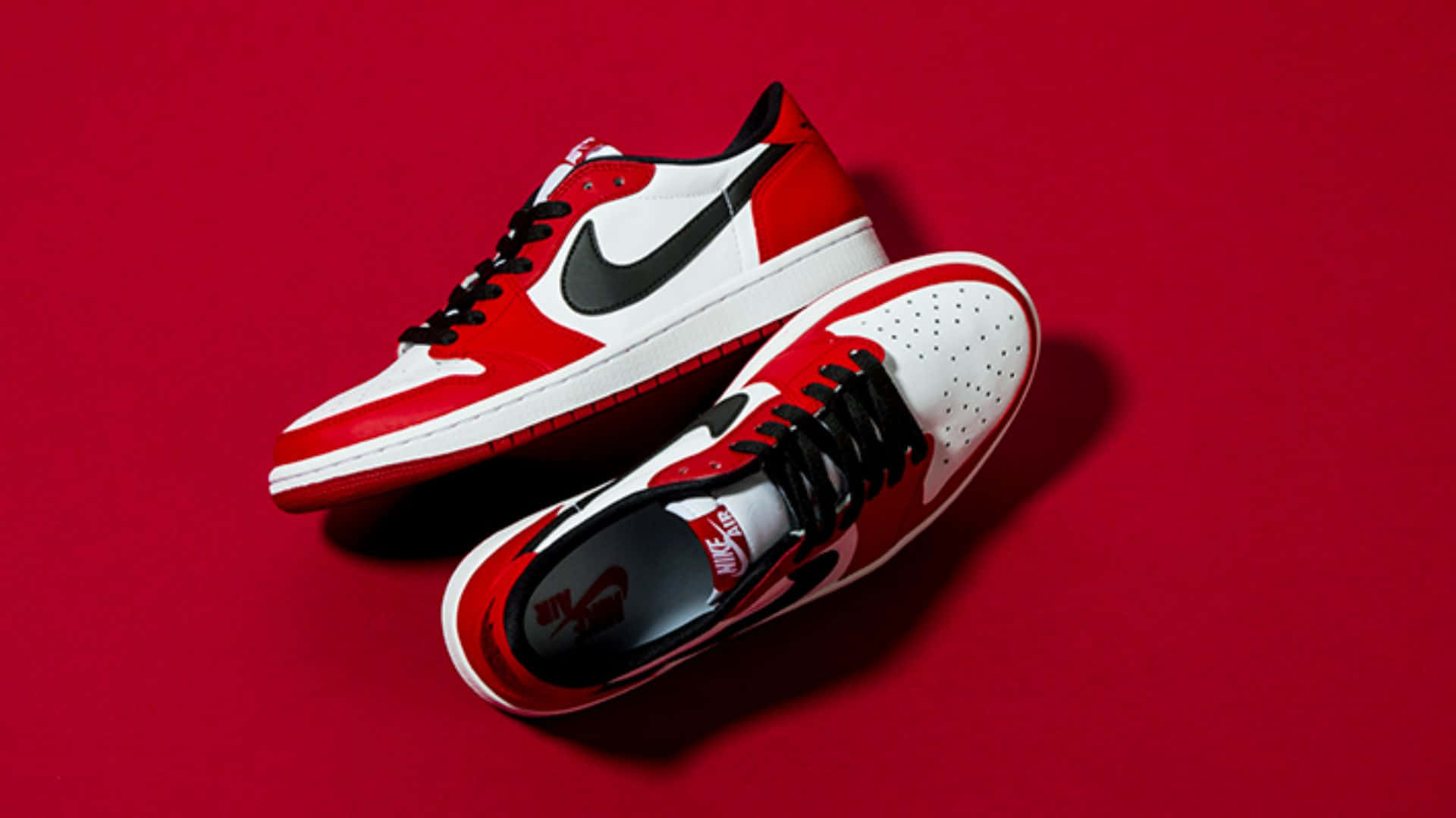 Air Jordan 1 桌布 壁紙 — 一雙紅白黑色的Nike Air Jordan運動鞋以傾斜角度放置在純紅色背景上，帶有柔和陰影。