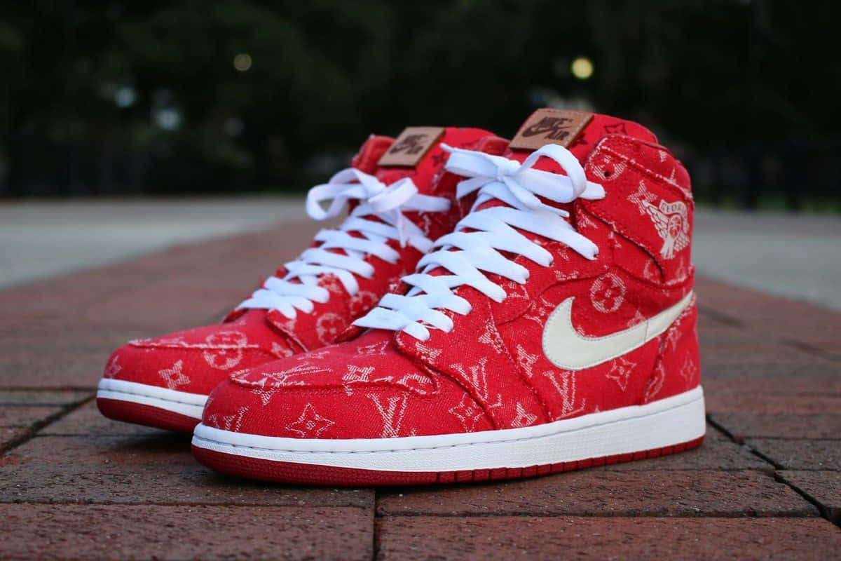 邁克爾·喬丹 桌布 壁紙 — 一雙紅色 Louis Vuitton x Nike Air Jordan 1 高筒鞋，搭配白色鞋帶和鞋底，放置在磚砌路面上。