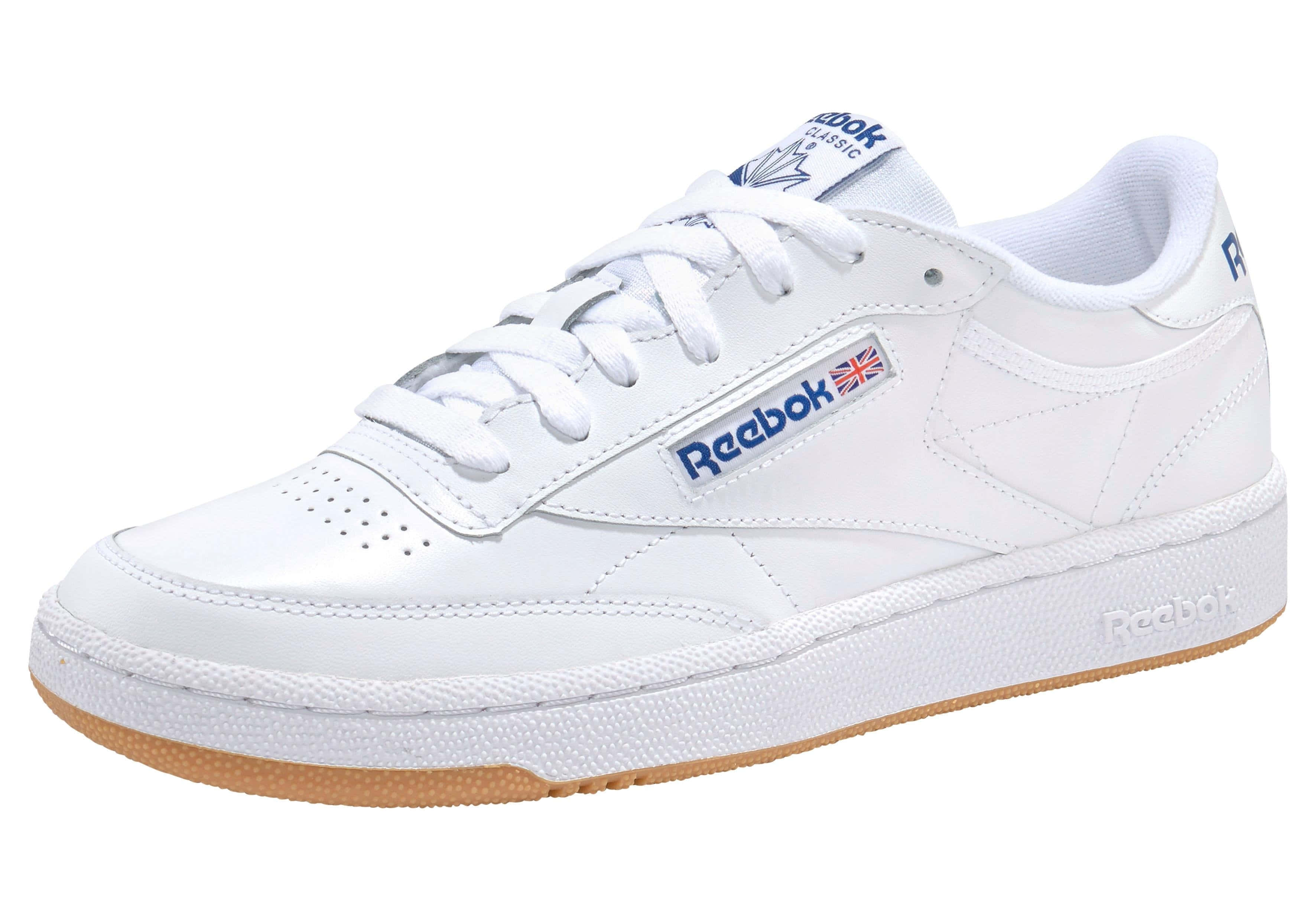 Reebok 桌布 壁紙 — 一雙純白色的 Reebok Classic 運動鞋，帶有藍色品牌標誌和棕褐色橡膠鞋底，在工作室燈光下展示。