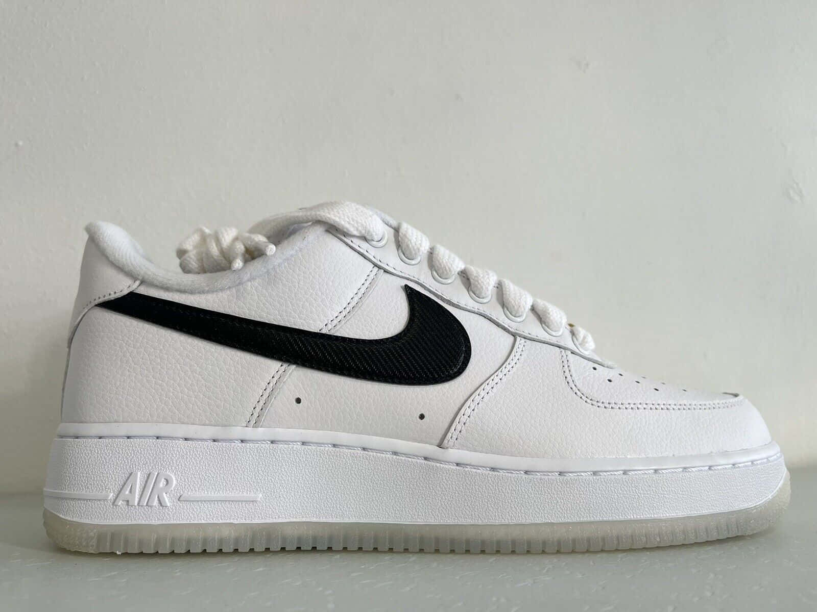 Nike Air Force 桌布 壁紙 — 一雙純白色的Nike Air Force 1運動鞋，帶有醒目的黑色Swoosh，靠在純色的米白色牆上。