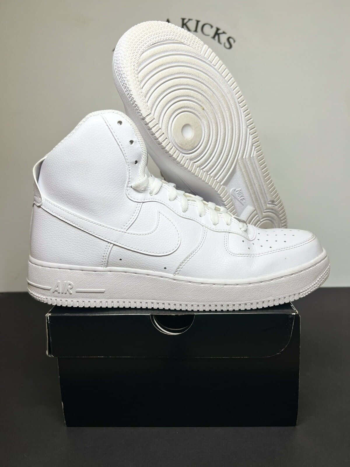 Nike Air Force 桌布 壁紙 — 一雙純白色的Nike Air Force 1高筒運動鞋直立展示在其黑色鞋盒上，鞋底面向觀眾。