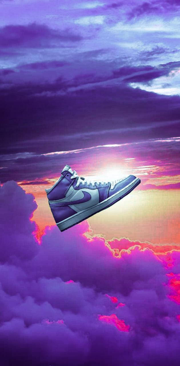 Nike Air Jordan 1 桌布 壁紙 — 一雙紫色和白色的高筒運動鞋漂浮在充滿活力的紫色和粉紅色雲層之上，背景是閃耀的日落天空。