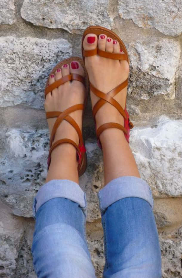 Sandals 桌布 壁紙 — 一雙腳穿著棕色綁帶涼鞋，塗著紅色指甲油，背景是粗糙的石牆，特寫鏡頭。