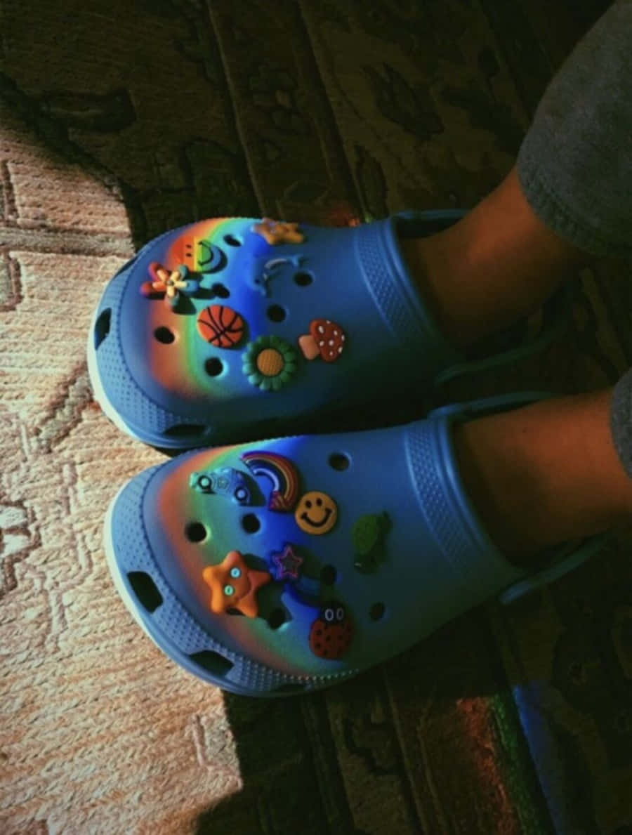 Crocs 桌布 壁紙 — 一雙藍色Crocs鞋，裝飾著彩色吊飾，放在圖案地毯上，室內燈光溫暖。
