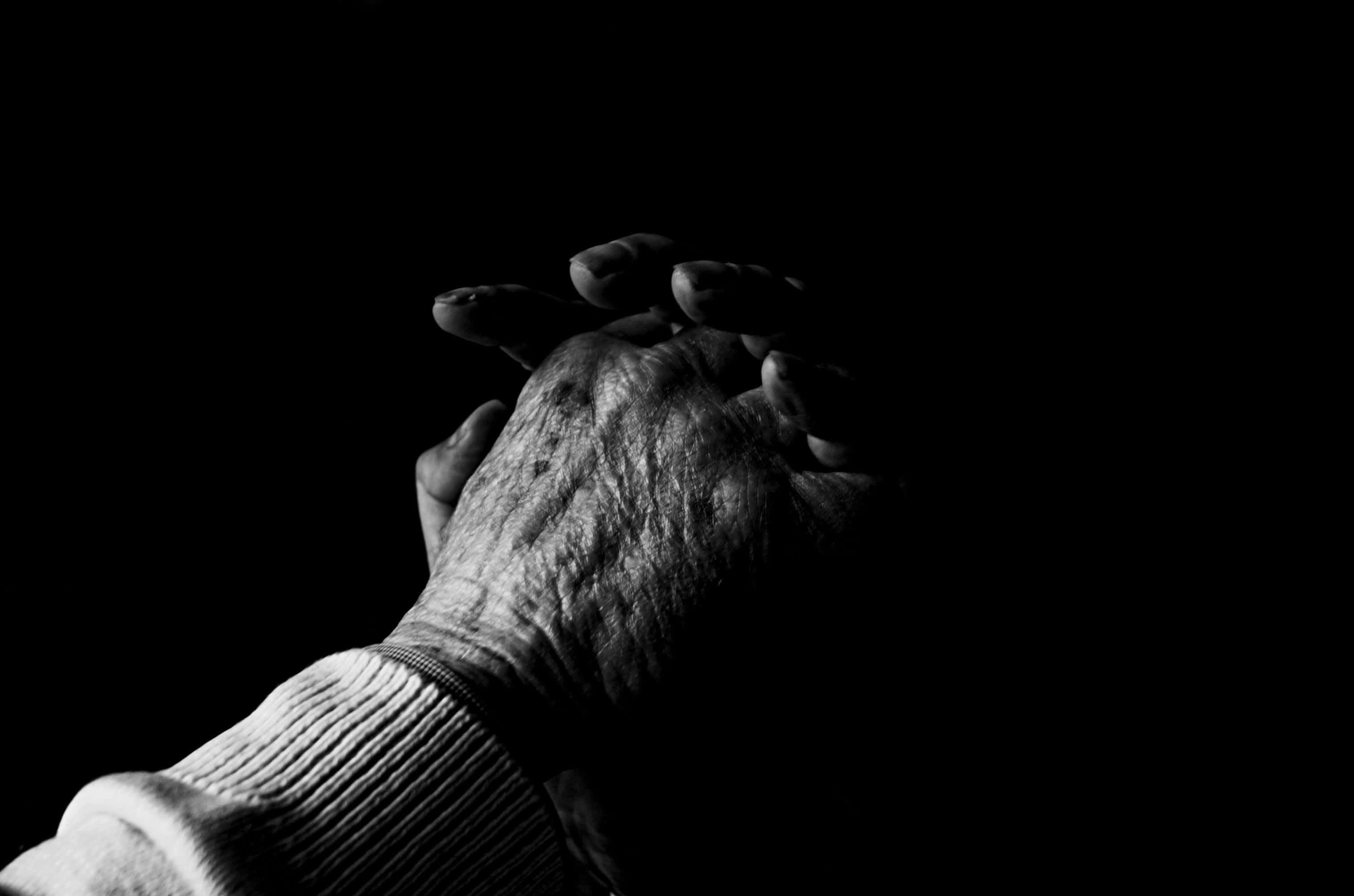 hands 桌布 壁紙 — 一雙長者滿是皺紋的手緊握在一起，背景為純黑色。