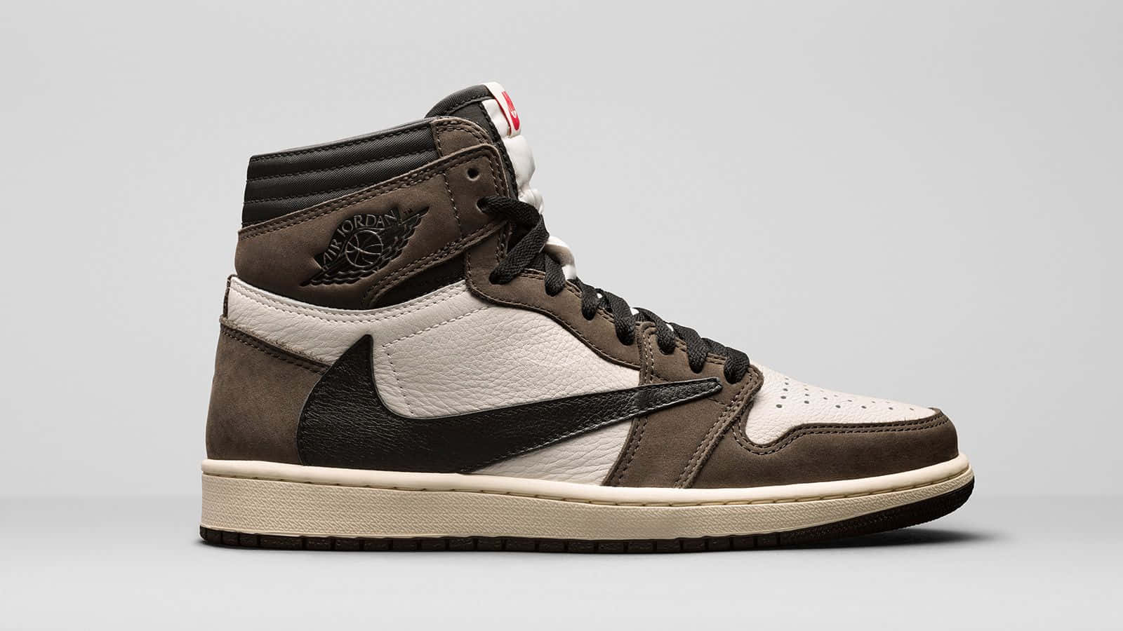 Travis Scott Jordan 1 桌布 壁紙 — 一雙高筒Jordan運動鞋，採用棕米色和黑色皮革，白色鞋底，純灰色背景。
