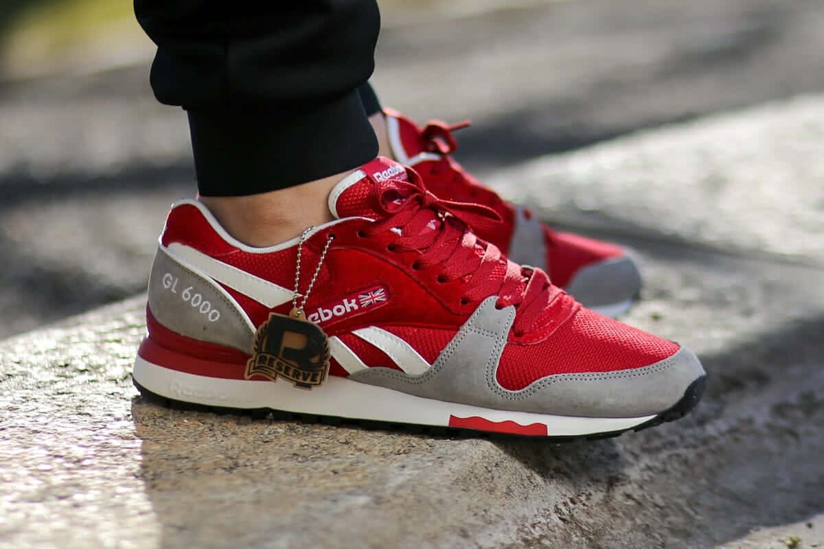 Reebok 桌布 壁紙 — 一雙鮮紅色Reebok運動鞋的特寫，帶有灰色點綴和「GL 6000」標籤，放置在紋理石鋪路面上。