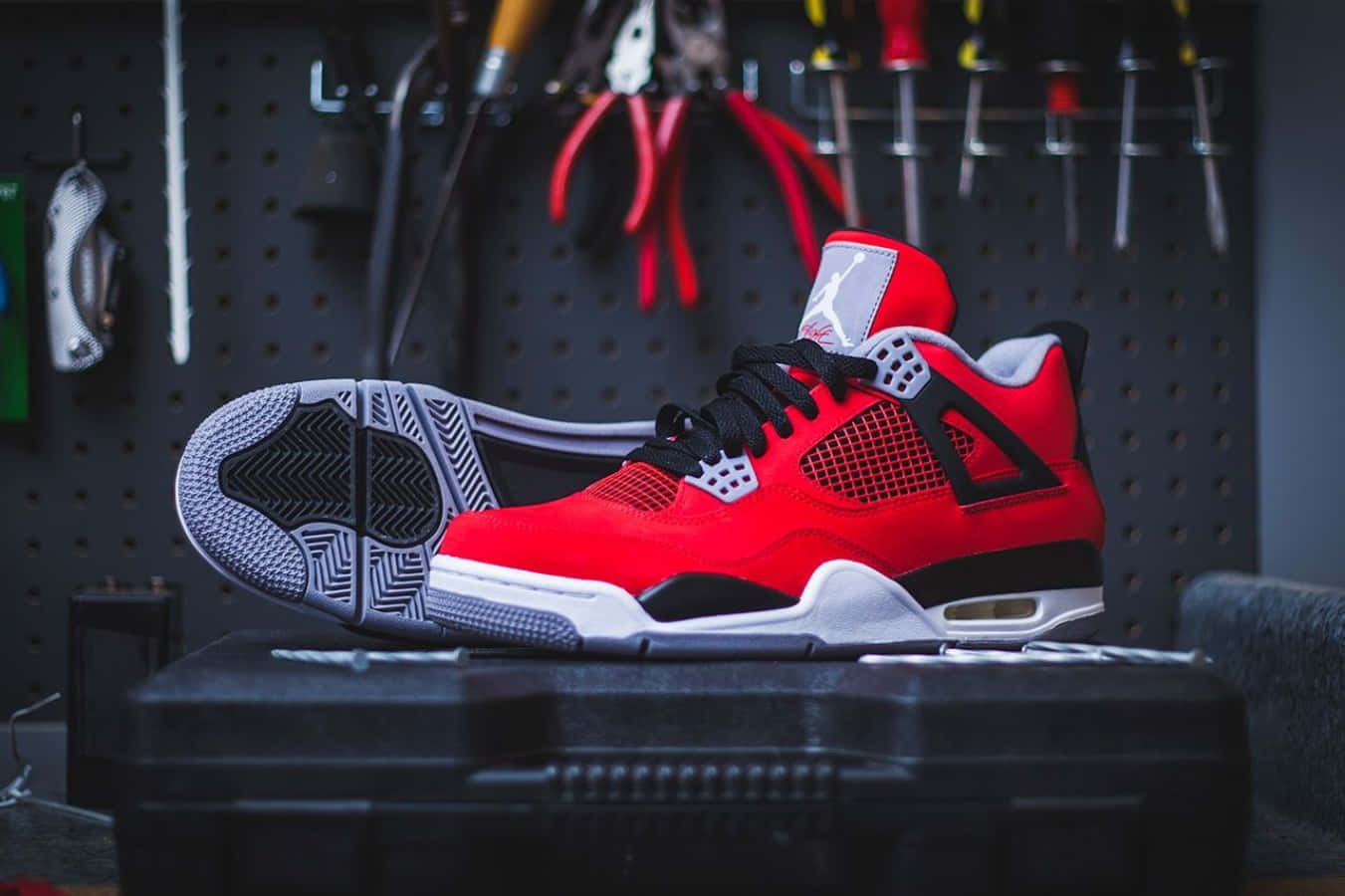 Air Jordan 桌布 壁紙 — 一雙鮮紅色的Jordan 4球鞋放在黑色工具箱上，背景是掛滿工具的深色洞洞板牆。