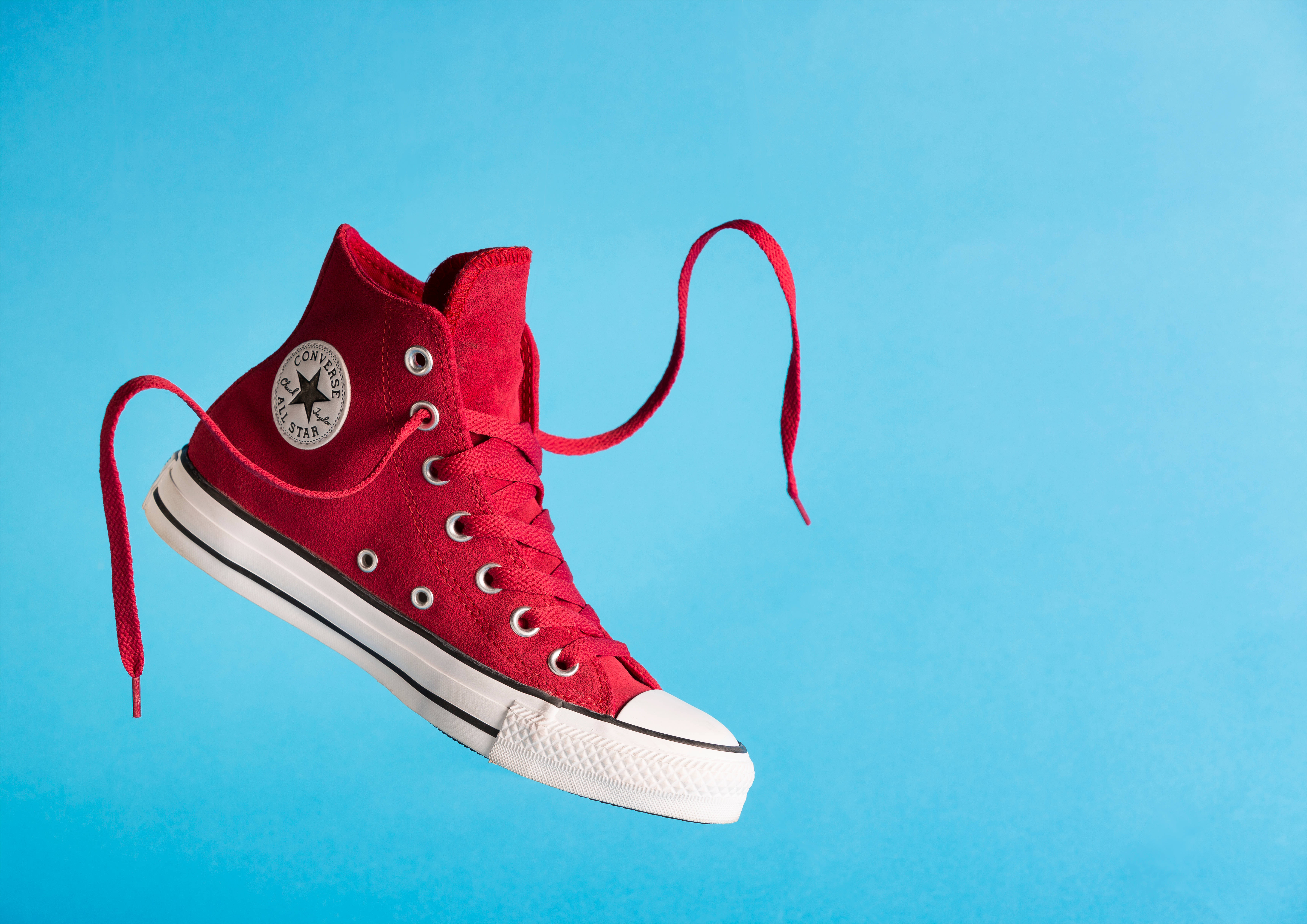 Converse 桌布 壁紙 — 一雙鮮紅色高筒Converse運動鞋在純藍色背景前懸浮於半空中，鞋帶未繫。