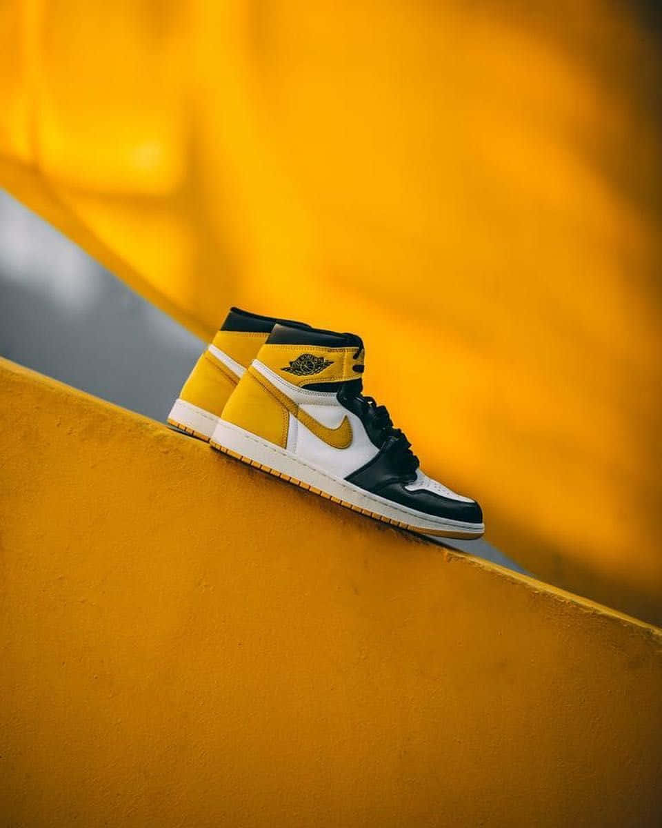 Yellow Jordan 桌布 壁紙 — 一雙黑、白、金色的Jordan 1運動鞋放在鮮黃色混凝土邊緣上，背景是模糊的金色。