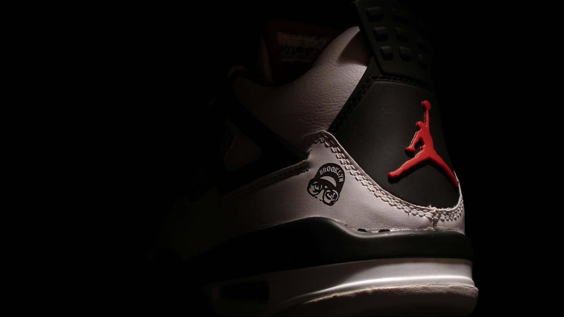Sneaker 桌布 壁紙 — 一雙黑白Jordan運動鞋的特寫，紅色Jumpman標誌在黑暗背景中發光。