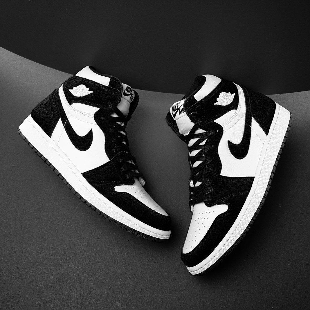 Nike Air Jordan 1 桌布 壁紙 — 一雙黑白高筒運動鞋，帶有標誌性勾勾和翅膀標誌，展示在深灰色彎曲表面上。