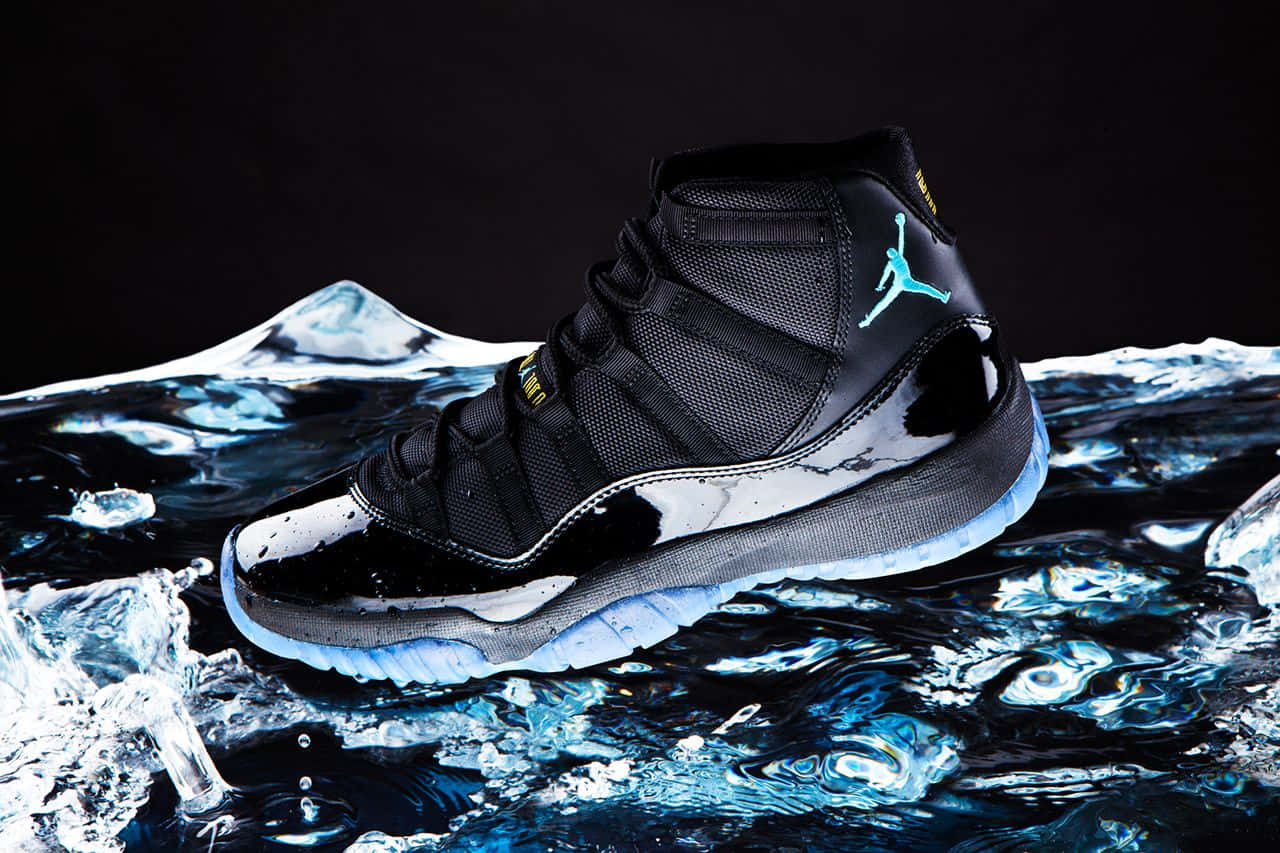 Air Jordan 桌布 壁紙 — 一雙黑色Jordan 11運動鞋帶有青綠色標誌，從飛濺的冰藍色水中浮現，背景為深色。