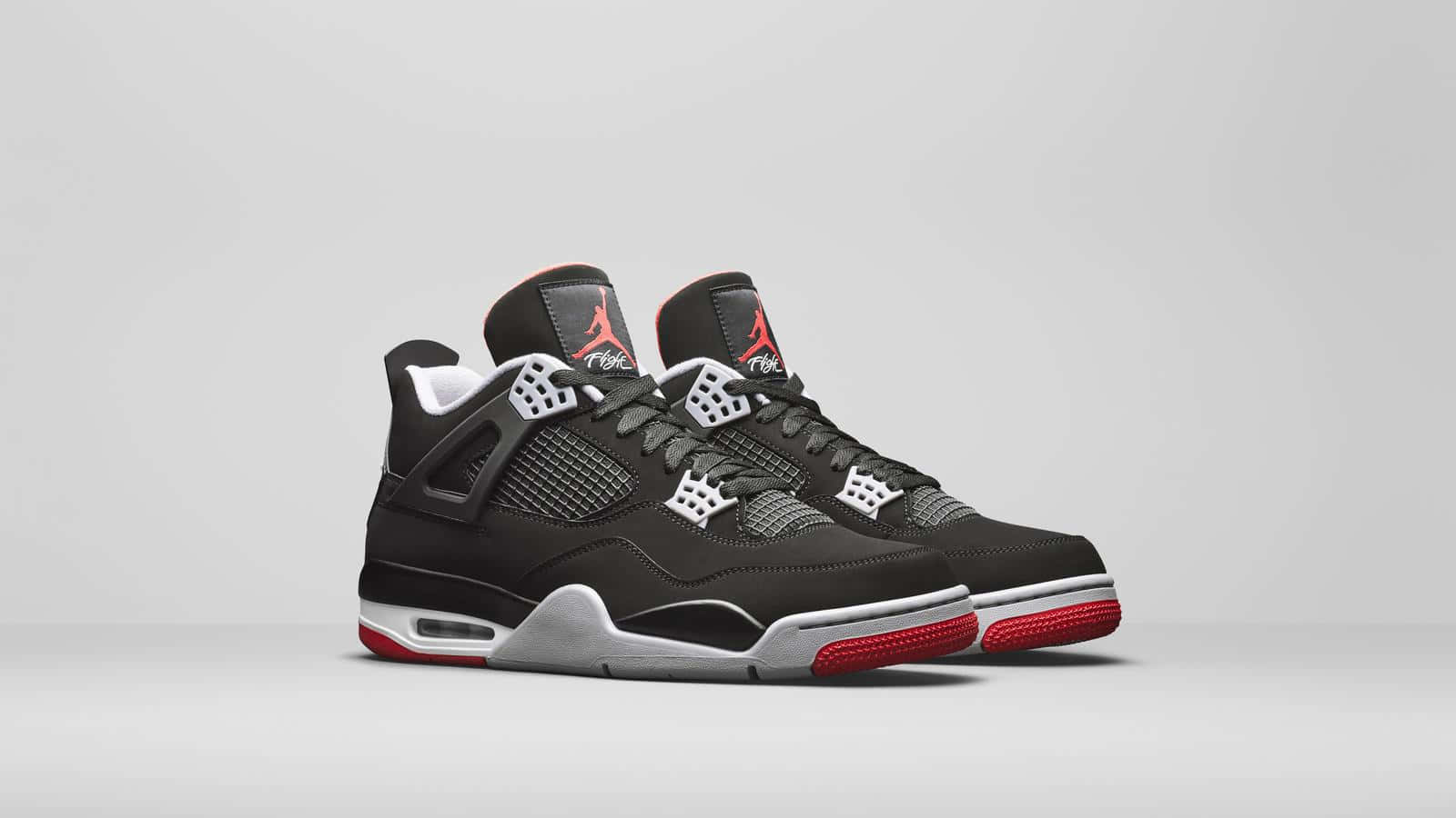 Air Jordan 桌布 壁紙 — 一雙黑色Jordan 4運動鞋，帶有紅色點綴和白色鞋底，展示在極簡灰色背景上。