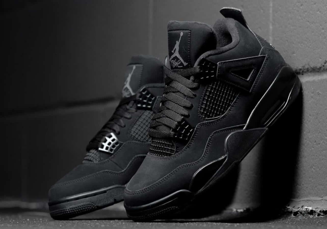 Sneaker 桌布 壁紙 — 一雙黑色Jordan 4運動鞋靠在混凝土牆上，在戲劇性的單色燈光下。