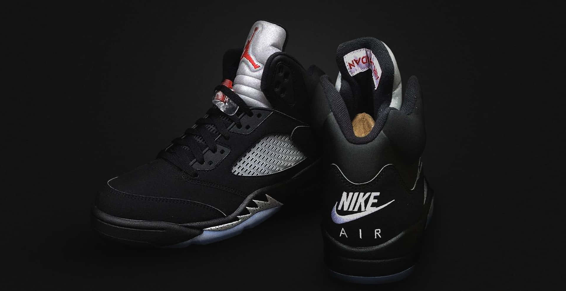 黑色 桌布 壁紙 — 一雙黑色Jordan 5運動鞋，帶有銀色點綴和紅色Jumpman標誌，在深色背景下展示。