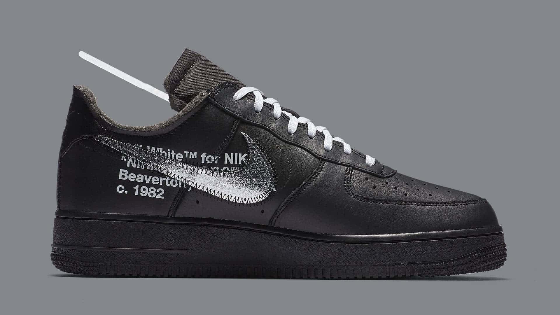 Black Air Force 桌布 壁紙 — 一雙黑色Nike Air Force 1運動鞋，配有白色鞋帶和銀色勾勾，帶有文字和拉鍊細節，背景為灰色。