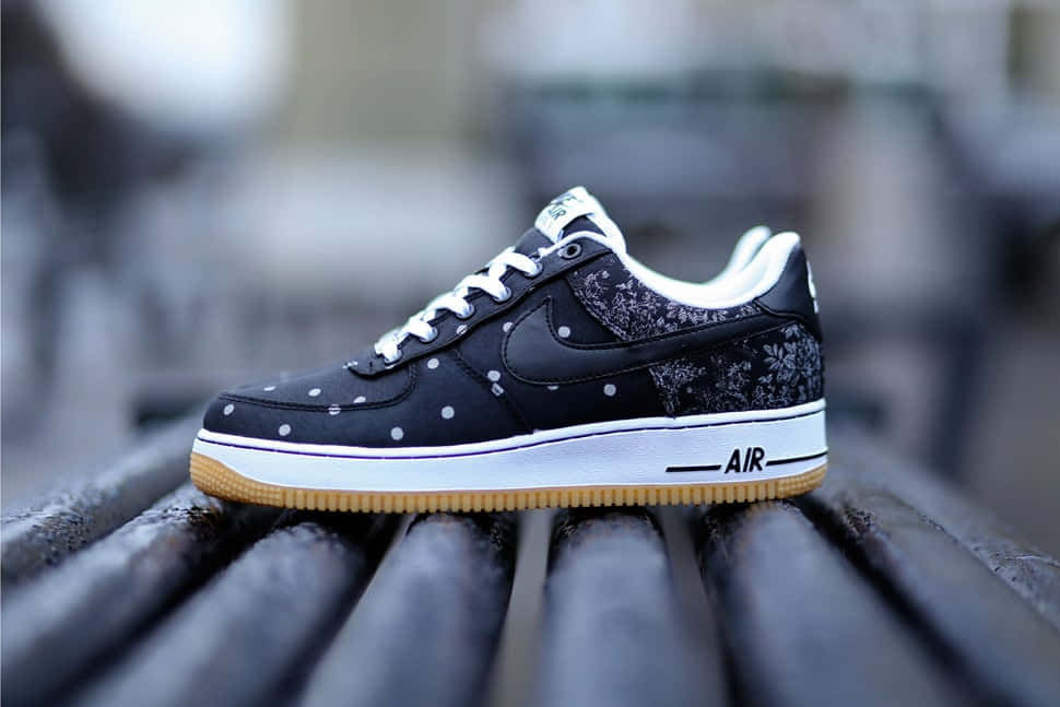Black Air Force 桌布 壁紙 — 一雙黑色Nike Air Force 1運動鞋，帶有白色圓點和花卉圖案，放在深色木長凳上。