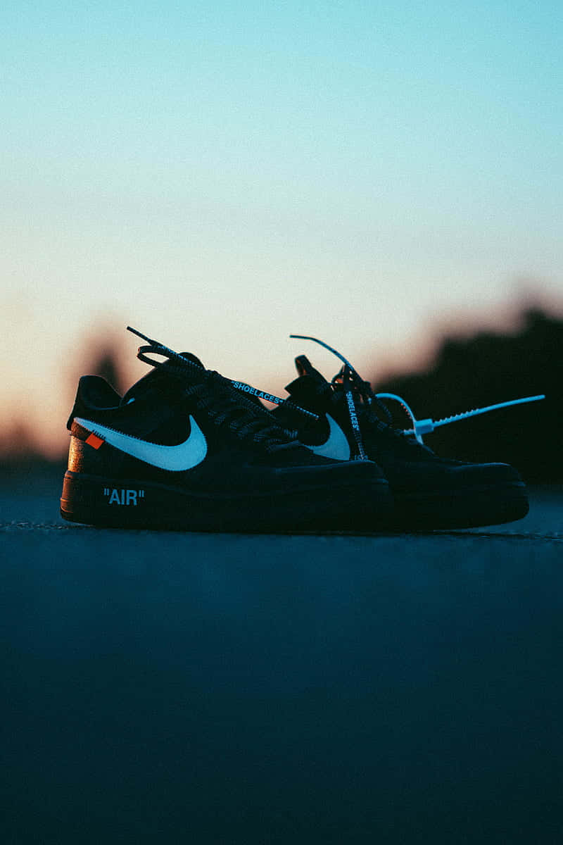 Black Air Force 桌布 壁紙 — 一雙黑色Nike Air Force 1運動鞋，帶白色swoosh和橙色標籤，放在窗台上，背景是暮色天空。