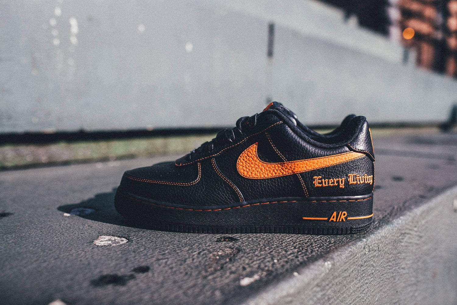 Vlone 桌布 壁紙 — 一雙黑色Nike Air Force 1運動鞋，帶有鮮豔的橙色點綴和「Every Living」字樣，在溫暖的陽光下放置於粗糙的城市人行道上。