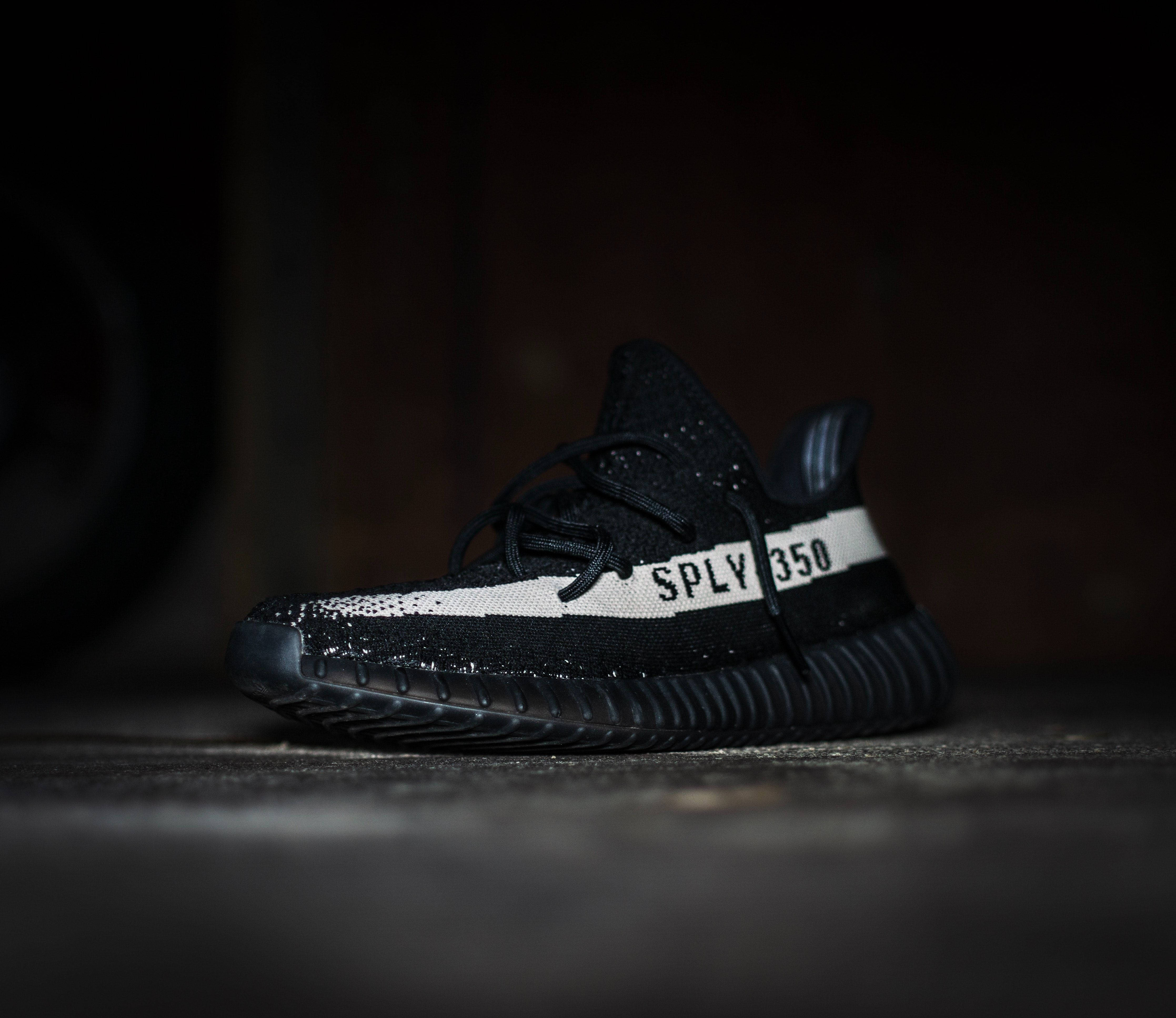 Sneakers 桌布 壁紙 — 一雙黑色Yeezy Boost 350運動鞋，帶有白色「SPLY 350」條紋，孤獨地放置在昏暗骯髒的城市環境中。