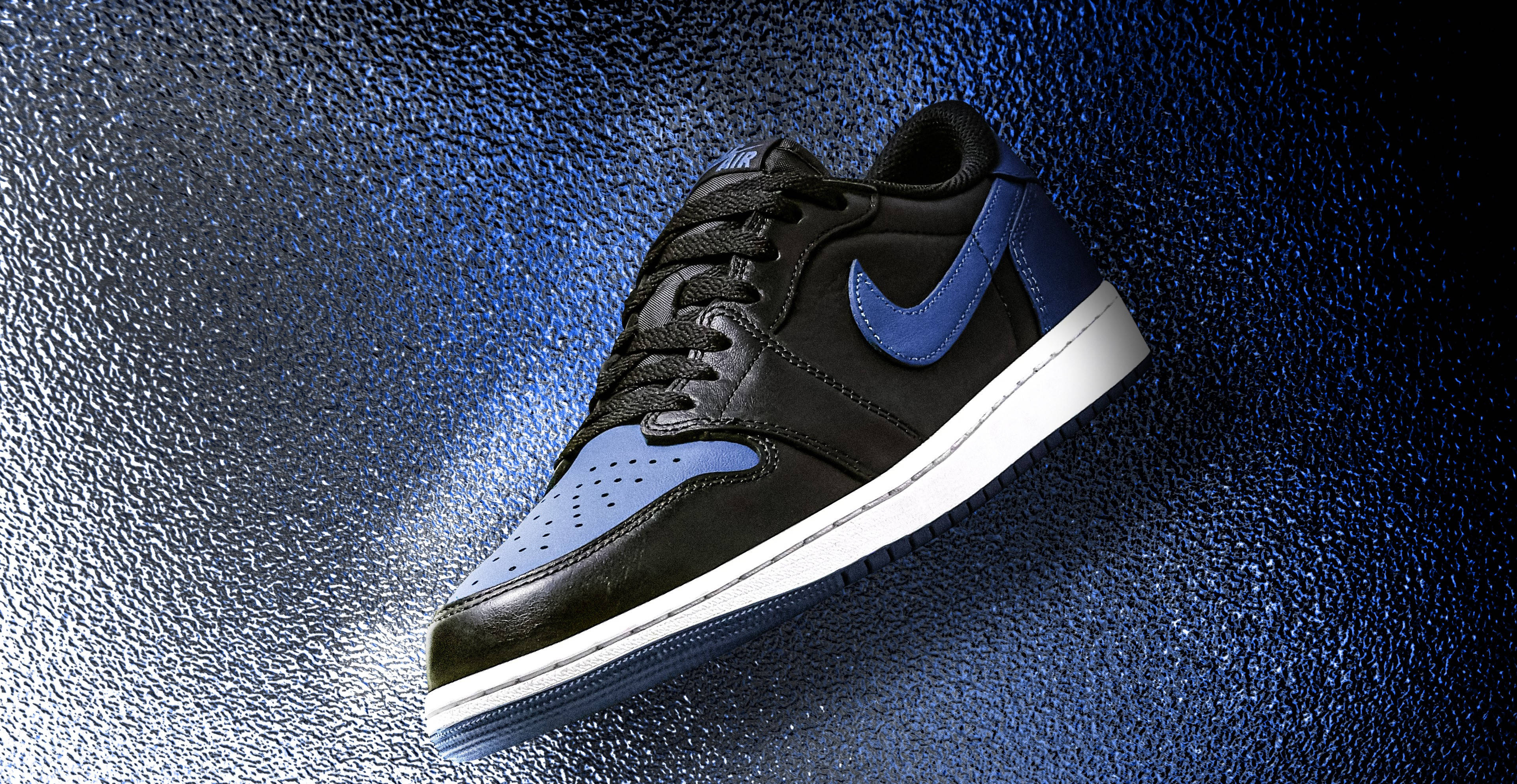 Air Jordan 桌布 壁紙 — 一雙黑色和藍色的Nike運動鞋，白色鞋底，在聚光燈下漂浮在帶有紋理的藍色背景上。