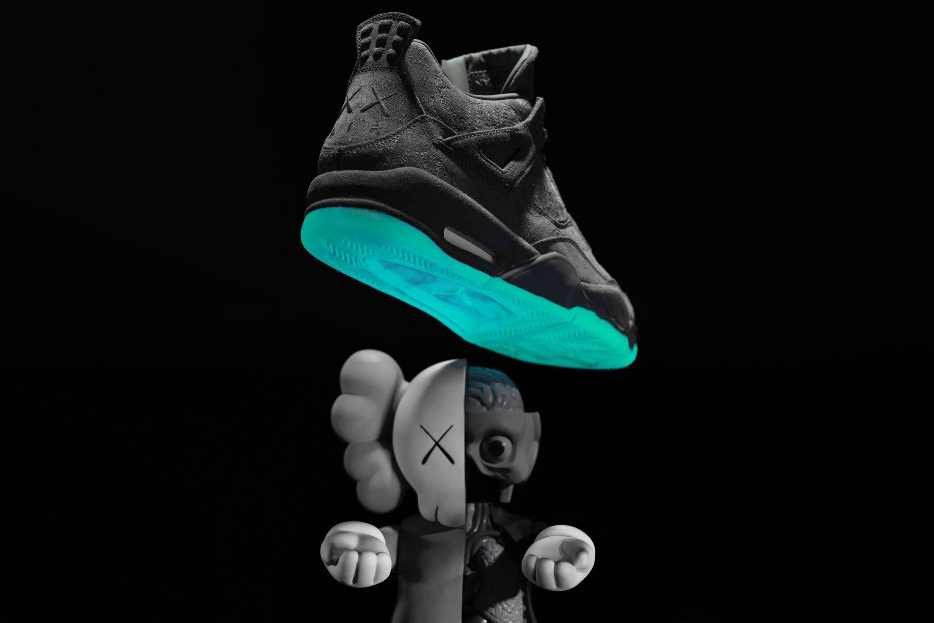 KAWS 桌布 壁紙 — 一雙黑色運動鞋帶有發光青色鞋底，懸浮在黑色背景上的分裂面孔KAWS公仔上方。