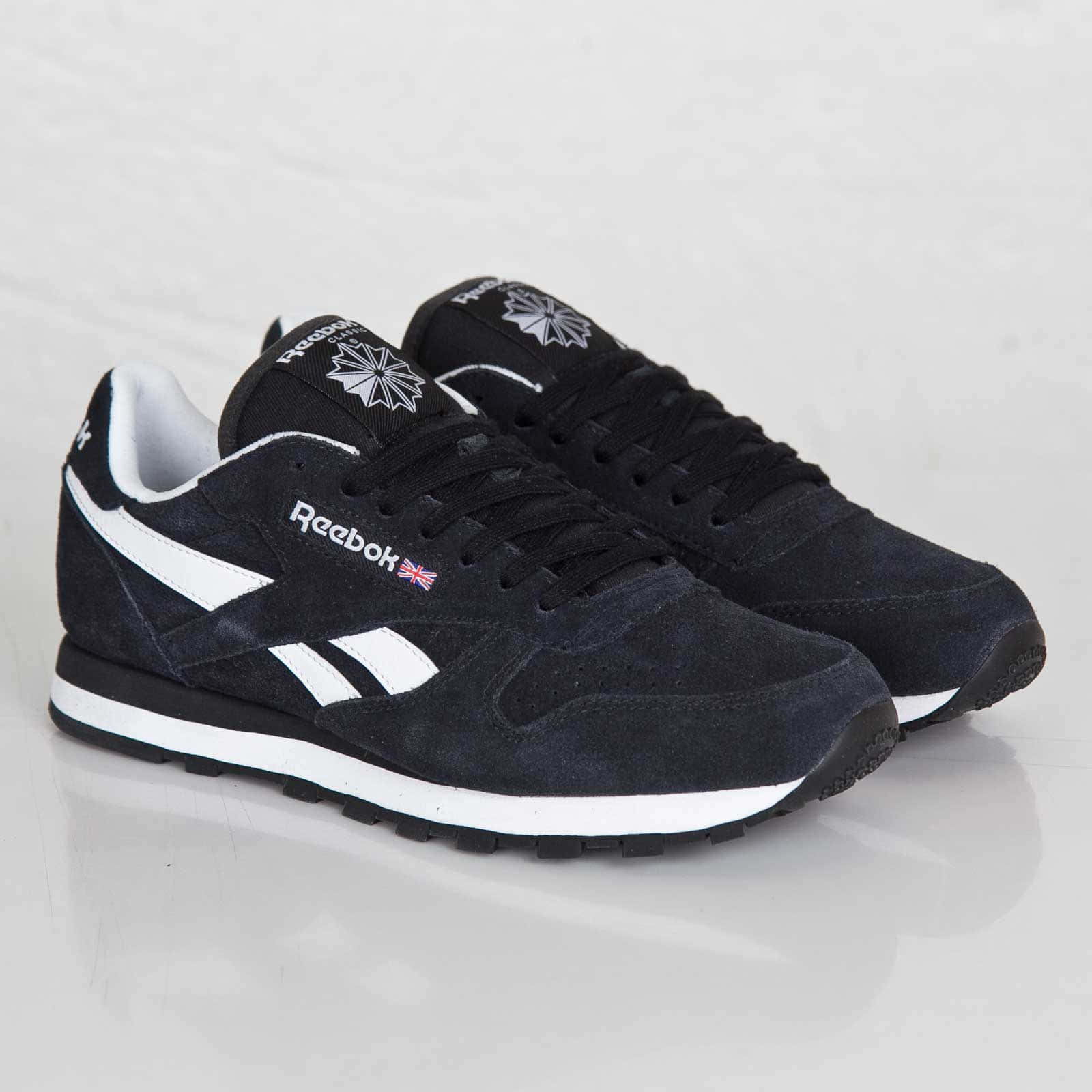 銳步 桌布 壁紙 — 一雙黑色麂皮Reebok運動鞋，帶有白色條紋和英國國旗細節，放在反光的白色表面上。