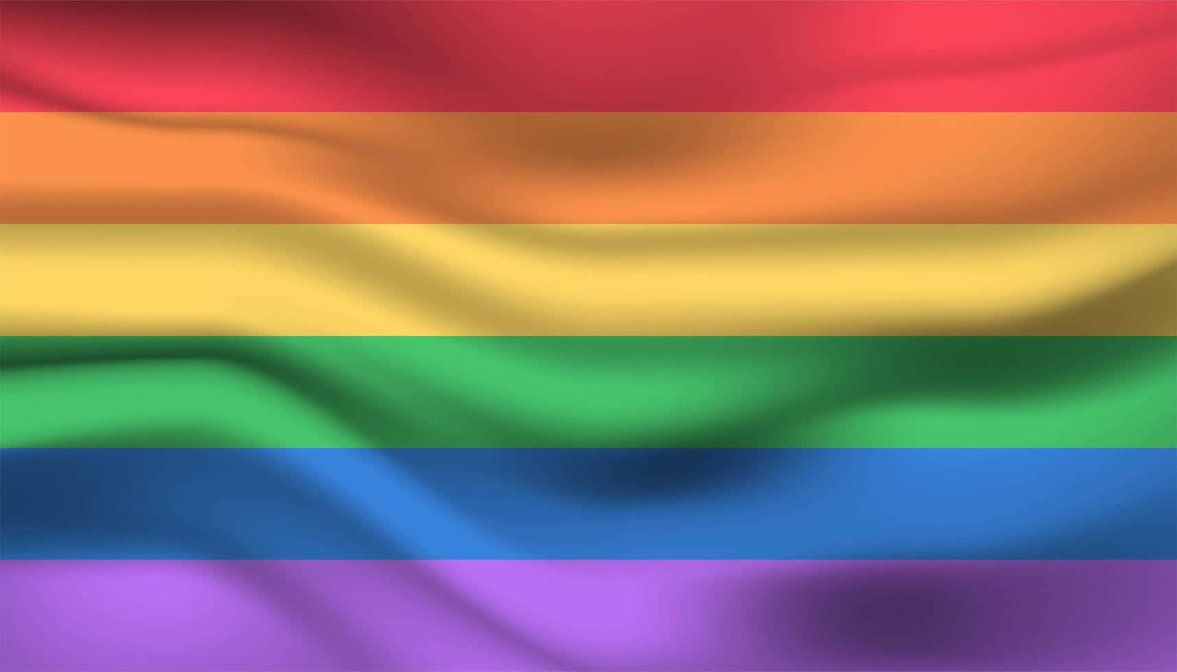 Pride Flag 桌布 壁紙 — 一面充滿活力的彩虹旗優雅飄揚，帶有柔軟的褶皺和豐富飽和的色彩，背景模糊。