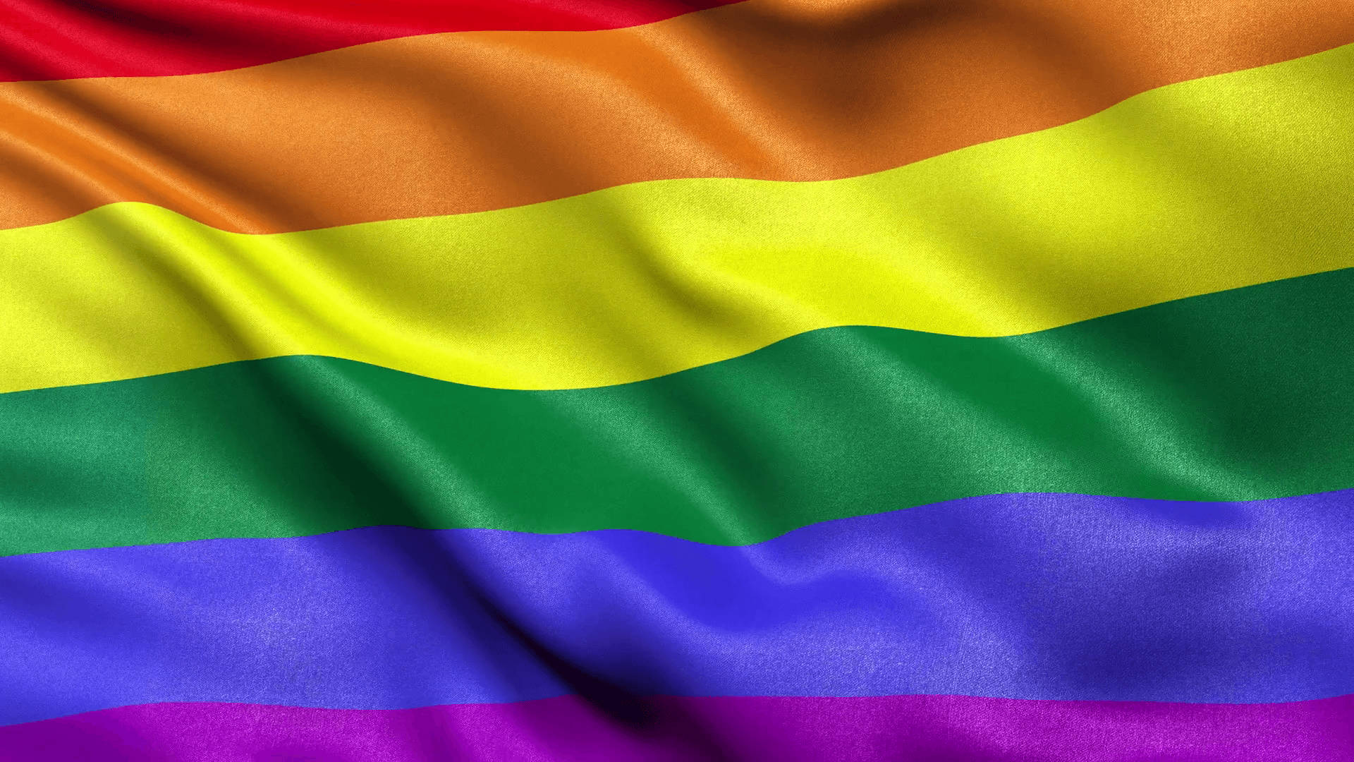 Pride Flag 桌布 壁紙 — 一面充滿活力的彩虹旗在明亮光線下飄揚，呈現豐富飽和的色彩和緞面質感。