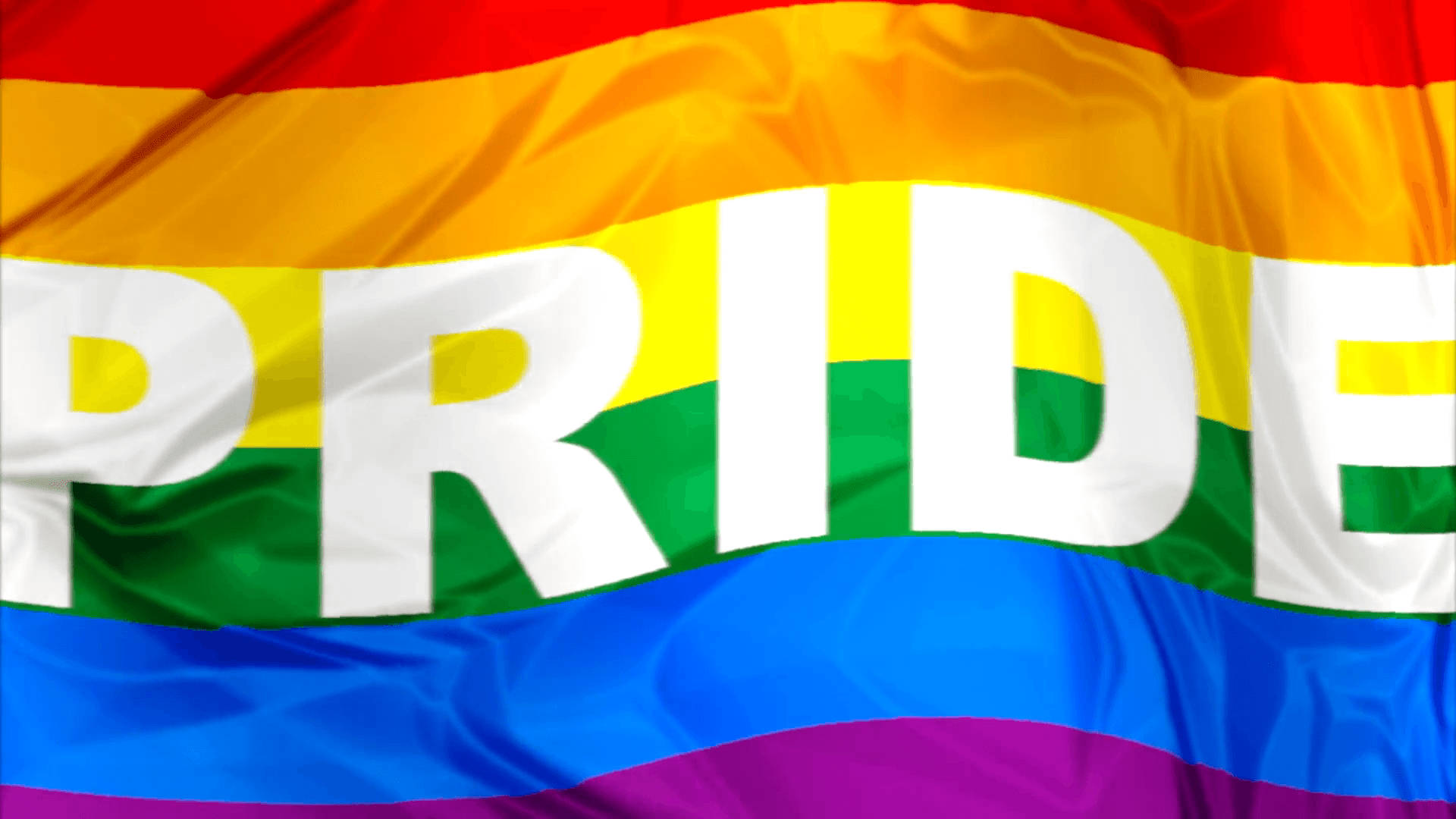 Pride Flag 桌布 壁紙 — 一面充滿活力的彩虹驕傲旗幟動態飄揚，粗體白色字母在其彩色條紋上拼寫出 PRIDE。