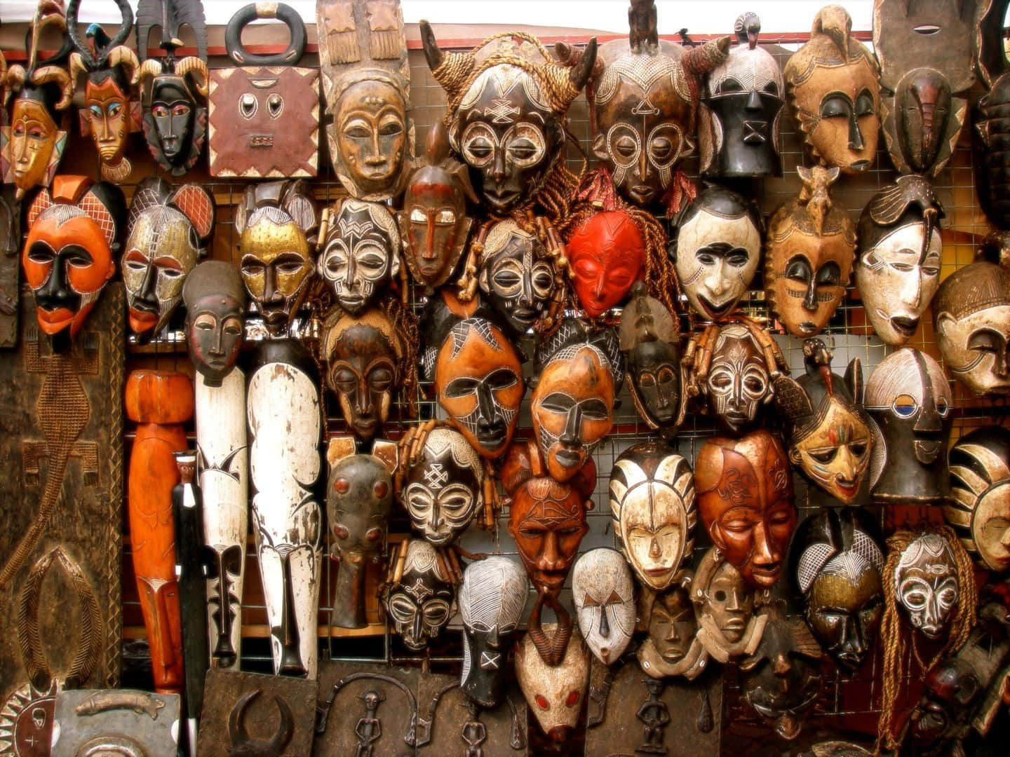 African Culture 桌布 壁紙 — 一面充滿活力的牆壁，密密麻麻地覆蓋著各種手工雕刻的木製面具，採用大地色調和複雜設計。