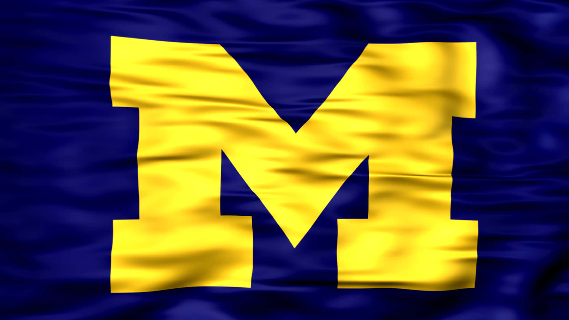Michigan Football 桌布 壁紙 — 一面充滿活力的藍色旗幟，上面有一個大膽的黃色塊狀 M，在風中動態飄揚。