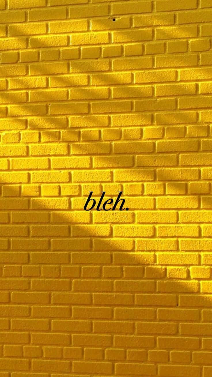 Brick Wall 桌布 壁紙 — 一面充滿活力的黃色磚牆，沐浴在陽光下，帶有樹葉陰影，中間以優雅字體寫著「bleh」。
